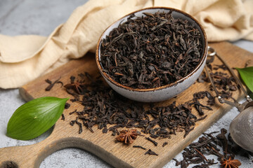 Bowl and wooden board with dry black tea leaves on grey background, closeup