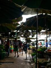 Obraz premium Blurred View of Shoppers at Local Market with Fresh Vegetables Stall.