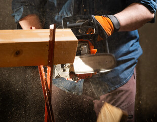 Worker uses a chainsaw to cut a plank into two pieces while working