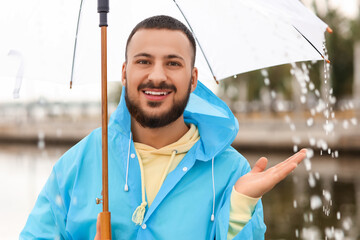 Young man in blue raincoat with umbrella on embankment