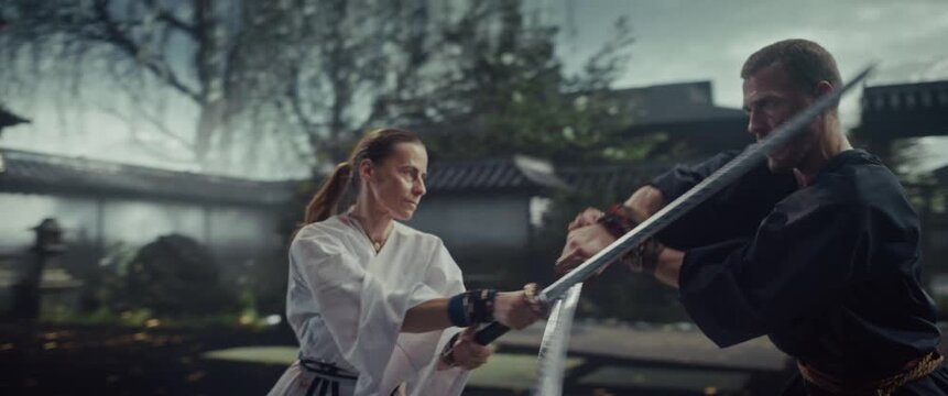 Sword Fight in Historical Japanese Attire with a Man and Woman Clashing Katanas Outside a Castle Gate. Calculated Movements Showing Authentic Martial Arts Technique. Slow Motion Cinematic Footage