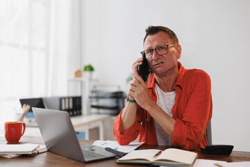 Businessman sitting at his desk in the office, receiving bad news during a phone conversation,...