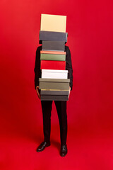 Person in black suit holding many boxes with hidden face on red background. Concept of Black Friday...
