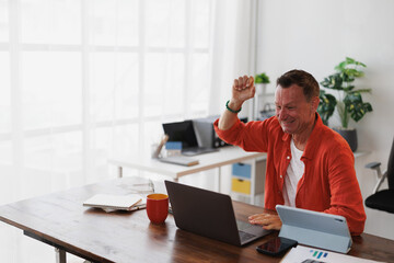 Happy businessman raising his fist in a gesture of triumph while sitting at his desk, celebrating a...