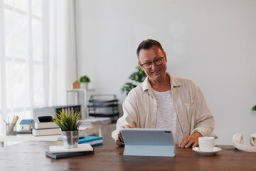 Happy businessman enjoying coffee while working remotely in a bright, modern home office filled with natural light and plants, enhancing productivity