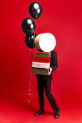 Person balancing boxes and black balloons while walking on red background. Concept of autumn...