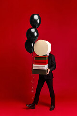 Person walking with gift boxes and black balloons on vivid red background. Concept of summer sale...