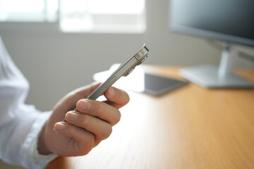 Hand Holding Smartphone on Wooden Desk — Side View, Bright Minimal Workspace