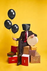 Businessman with black shopping bag on head sitting with balloons and gift boxes on yellow...
