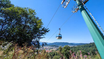 Mountain cable car climbing verdant slopes, revealing panoramic valley landscape under bright blue...