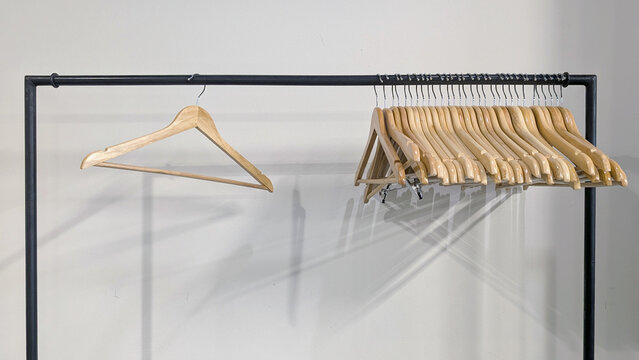Empty wooden hangers are hanging on a metal clothes rack rail, casting shadows on a white wall, representing fashion, retail, and wardrobe organization