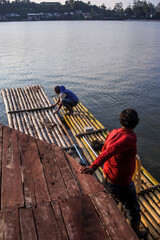 Two Fishermen Are on a Traditional Bamboo Raft, With one Standing on a Wooden Pier