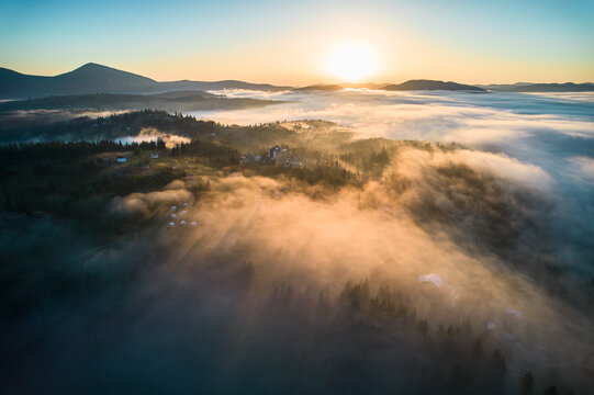 Fototapeta Stunning aerial view of sunrise over mountainous landscape, with thick fog blanketing valleys and hills. Sun's golden rays pierce through mist, casting serene glow over the entire scene.