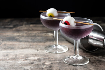 Purple Halloween cocktail garnished with candy eye on wooden table