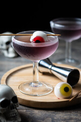 Purple Halloween cocktail garnished with candy eye on wooden table