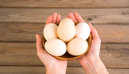 Hands holding eggs in bowl on wood