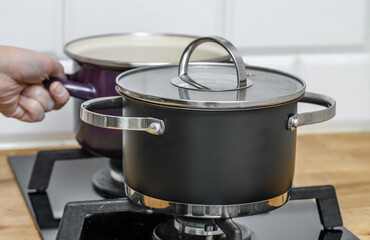 A man cooks dinner in two pots, one with a lid, the other without.