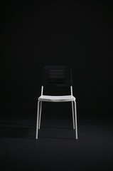 An empty modern white and black chair isolated on a dark background. A concept of solitude, waiting, or minimalist interior design