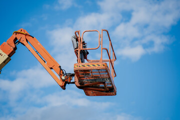 Elevated aerial work platform, orange boom lift with safety cage against sky, construction and...