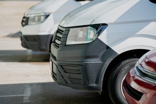 Commercial vehicles parked in line, close view of van fronts with bumper and light detail, modern automotive fleet for transport, delivery services, logistics operations, company vehicles on site