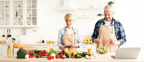 Adult couple prepare food together for family dinner. Smiling mature male and woman make salad in...