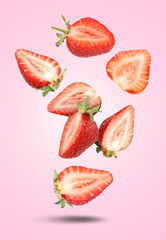 Cut fresh juicy strawberries falling on pink gradient background