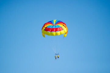 Two people glide through the sky while parasailing under a dazzling, multicolored parachute in Bulgaria