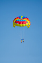 Two people glide through the sky while parasailing under a dazzling, multicolored parachute in Bulgaria