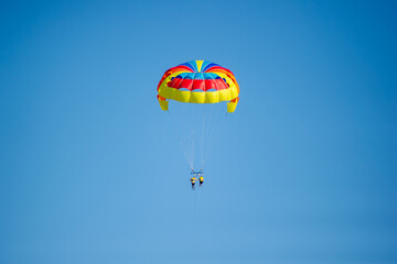 Two people glide through the sky while parasailing under a dazzling, multicolored parachute in Bulgaria