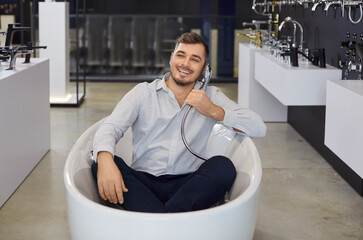 Funny sale manager helping to choose bathroom shower set sitting in bathtub, enjoy playing to...