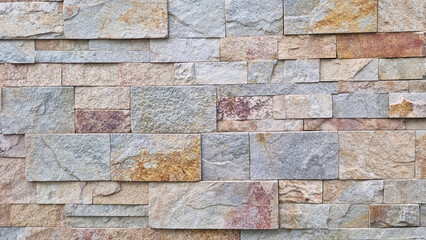 Pattern of rectangular natural stone tiles in mixed earthy tones forming a stacked wall texture. Stone cladding surface photography. Construction background concept
