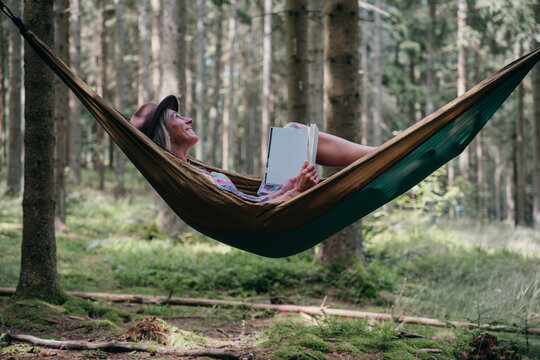 Relaxing in the forest, a woman reads a book in a hammock, enjoying silence, nature, and mindful freedom in the outdoors