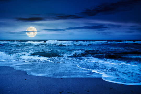 stormy sea landscape with splashing green waves under windy overcast sky with heavy cumulus clouds at night. spoiled summer vacations. bad weather strikes in full moon light