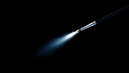 Fototapeta premium A paintbrush tip sprays a light blue mist against a black background