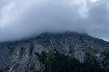 Dark mountain ridge shrouded in heavy clouds, dramatic alpine scene with dense evergreen forest below