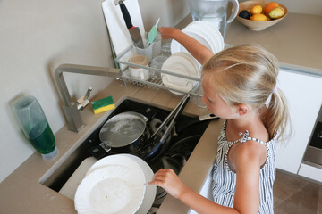 Girl rinsing fork with sponge under running water at sink
