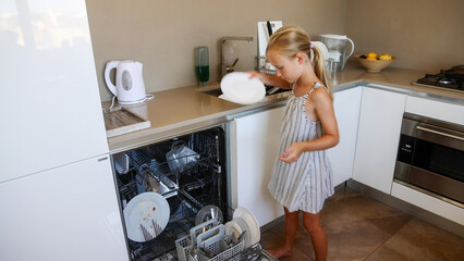 Girl loading dirty plates into dishwasher in kitchen