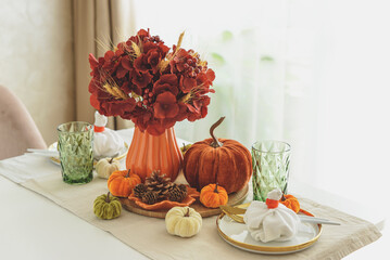 Thanksgiving table setting with decorative pumpkins, candles and string lights on white wooden table