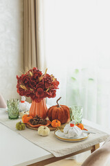 Thanksgiving table setting with decorative pumpkins, candles and string lights on white wooden table