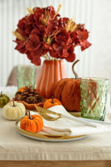 Thanksgiving table setting with decorative pumpkins, candles and string lights on white wooden table