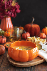 Creamy pumpkin soup with croutons and seeds, served in a pumpkin-shaped bowl on dark wooden table.