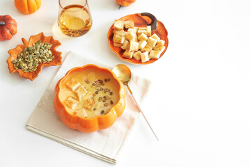Creamy pumpkin soup with croutons and seeds, served in a pumpkin-shaped bowl on white wooden table. Top view