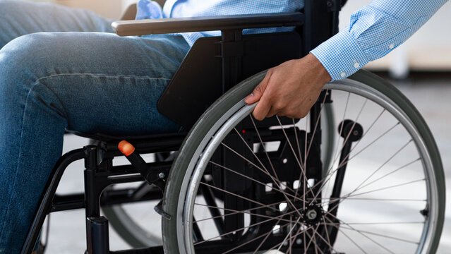 Cropped view of with disability black man sitting in wheelchair at home. Unrecognizable young guy using medical equipment indoors. Impairment and mobility aids concept