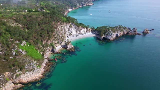 Drone flying forward towards Île Vierge Beach in Crozon Peninsula, Brittany, showing cliffs, turquoise sea, small boats, light mist, and coastal landscape - France