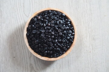 Coffee beans in wooden bowl on light background