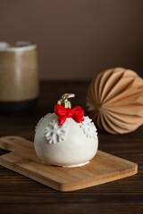 Christmas ball cake with a red bow and snowflakes on a wooden table. Vertical orientation.