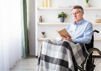 Senior impaired man in wheelchair reading book at home, full length portrait. Elderly handicapped...