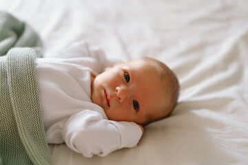 Newborn baby lying on bed under a soft blanket, capturing a moment of innocence and curiosity...