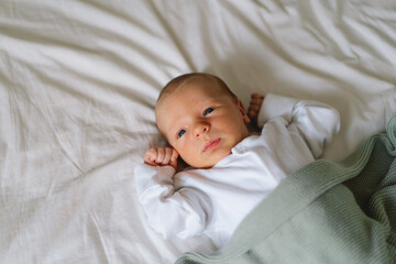 Newborn baby lying on bed under a soft blanket, capturing a moment of innocence and curiosity...
