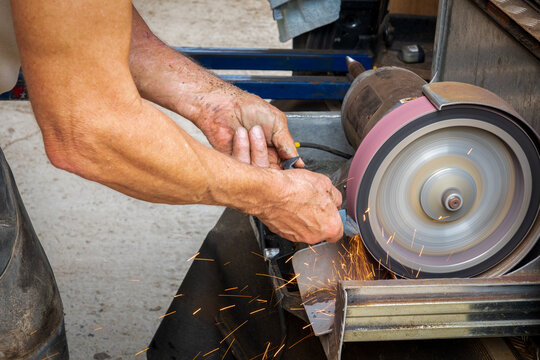 Farrier sharpening tool on electric grinding wheel sparks —metalwork, manual labor, skilled craftsmanship. - Powered by Adobe
